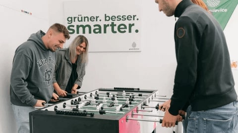 Vier greendevice business GmbH Mitarbeiter spielen gemeinsam Kicker während der Arbeit