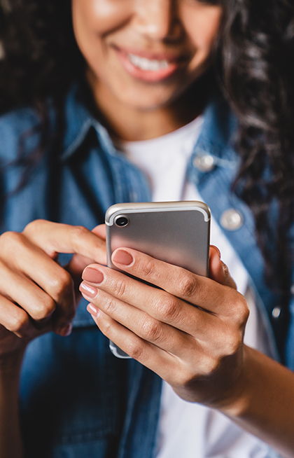 Cropped shot of an african-american young woman using smart phone at home. Smiling african american woman using smartphone at home, messaging or browsing social networks while relaxing on couch